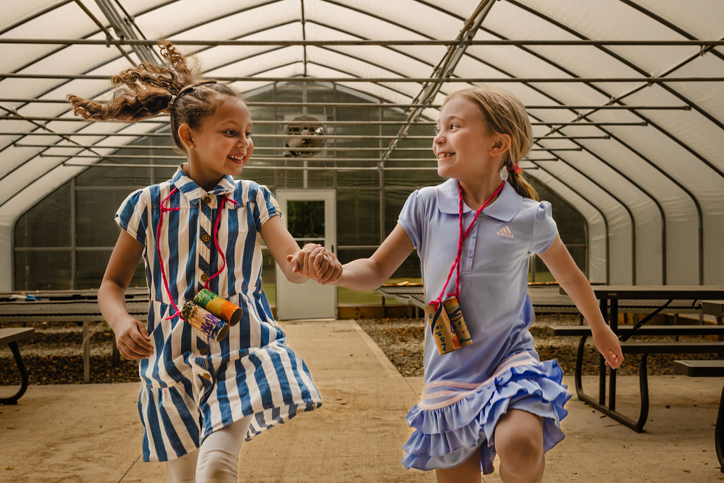 two girls holding hands and skipping in the greenhouse
